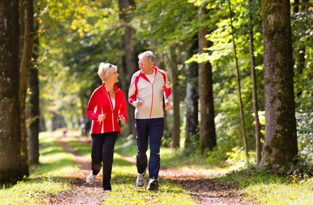 An older adult man and woman smiling while jogging outdoors.