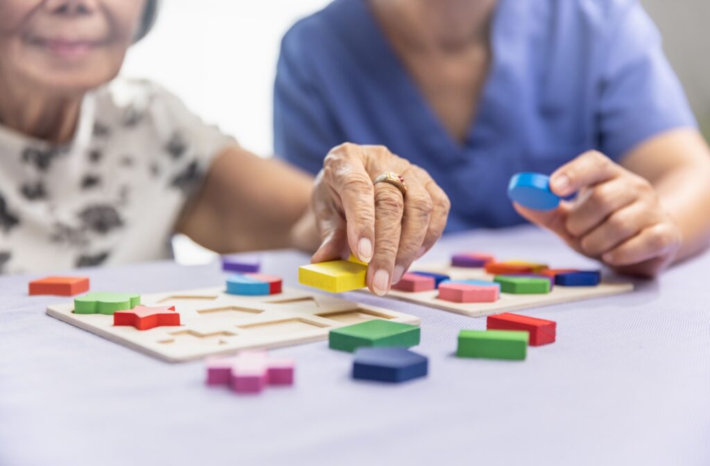 An older adult woman and an aide play a wooden shape game in a memory care community to help strengthen cognitive function.